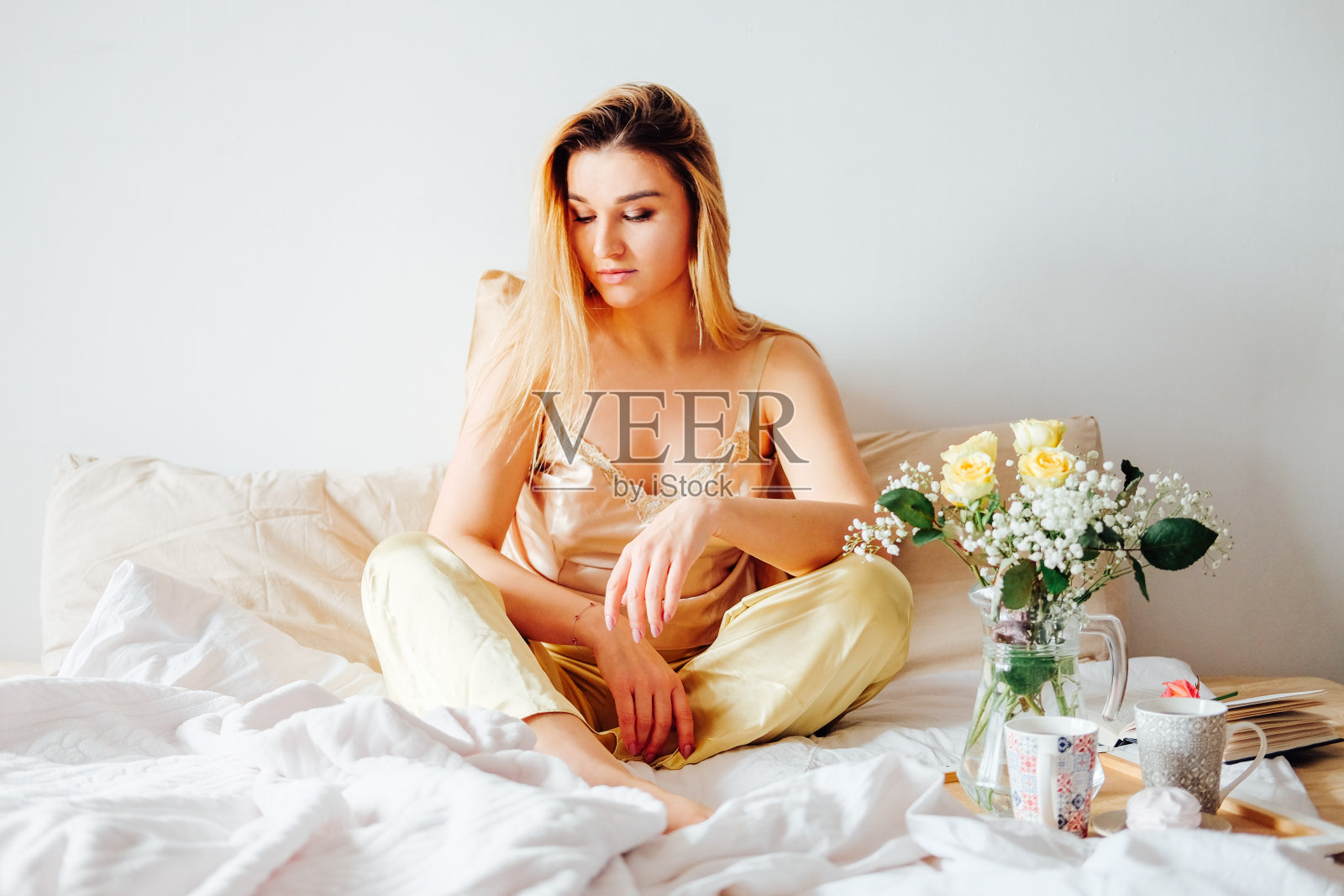 穿着黄色缎面睡衣的金发女人在床上享用早餐,感到舒适放松照片摄影图片