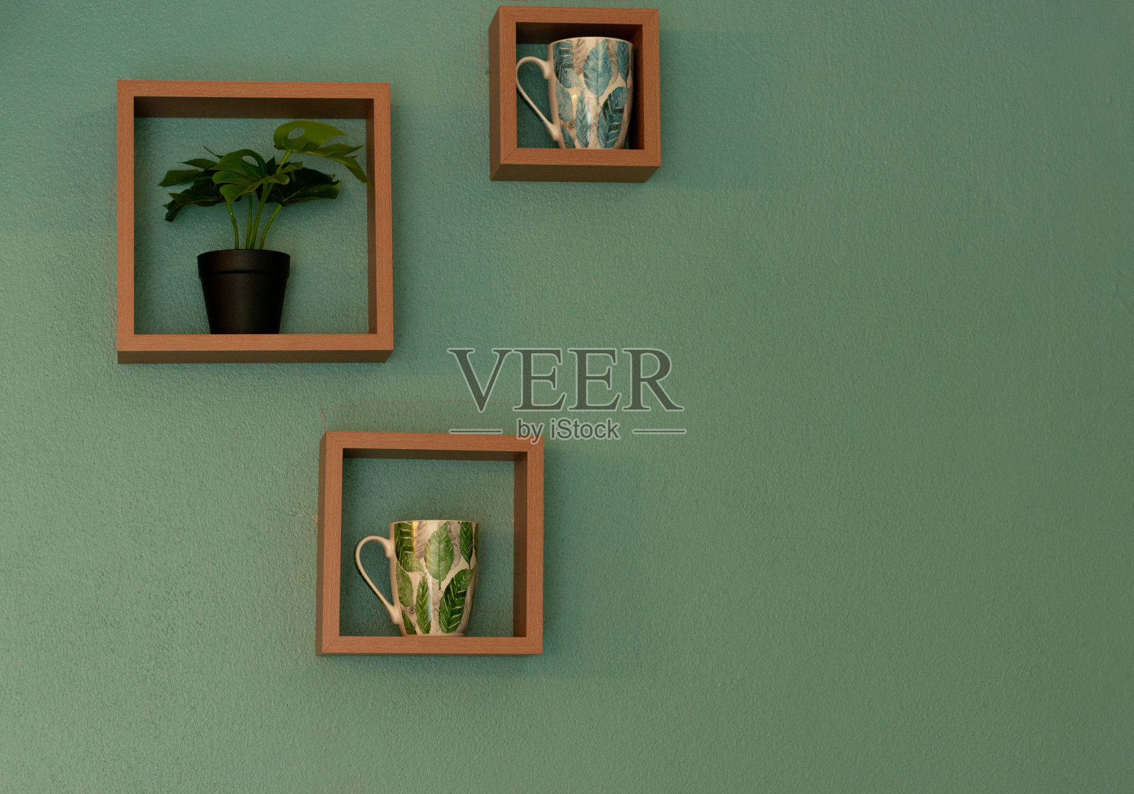木架子上挂着咖啡杯,绿色的墙上有棵小树。照片摄影图片