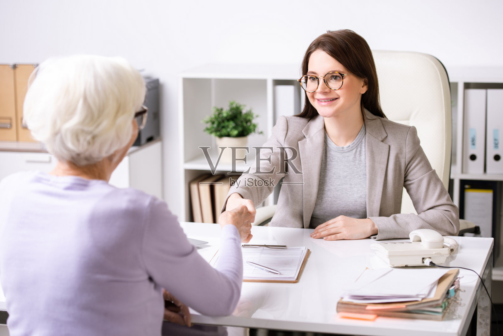 年轻有为的经纪人看着退休妇女并与她握手照片摄影图片