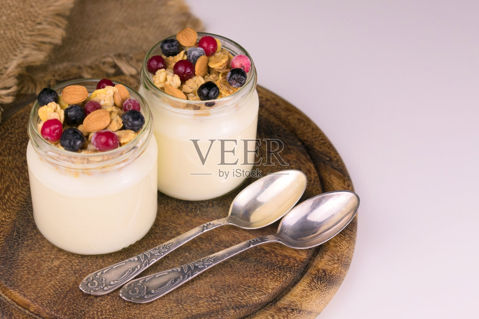 两份酸奶加麦片和浆果放在木板上。照片摄影图片