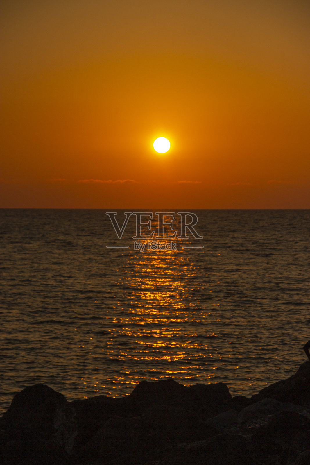 美丽的海上落日。海滩上美妙的夏日景色。炽热的日落景观在黑色的海洋和橙色的天空与可怕的太阳反射在平静的波浪。照片摄影图片