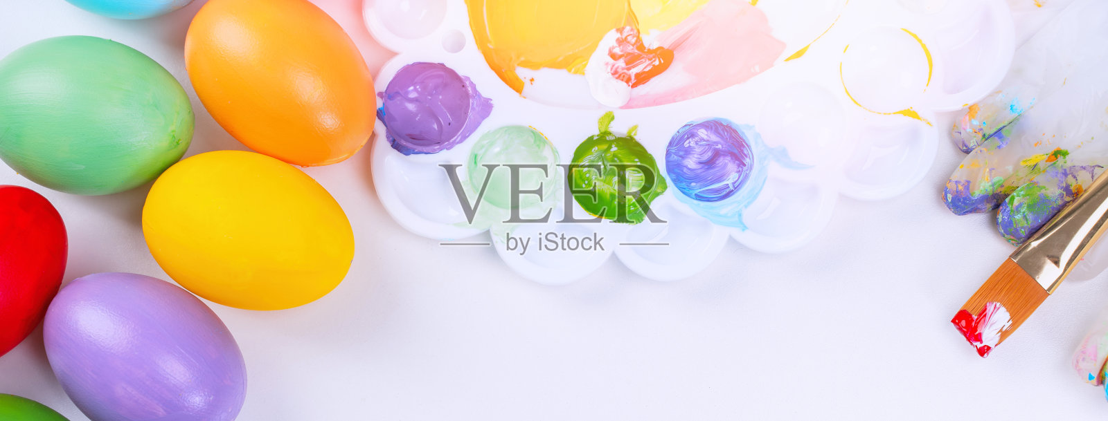 设计理念——准备复活节庆祝活动,用彩色丙烯酸颜料在调色板上画复活节彩蛋,俯视图,生活方式。照片摄影图片