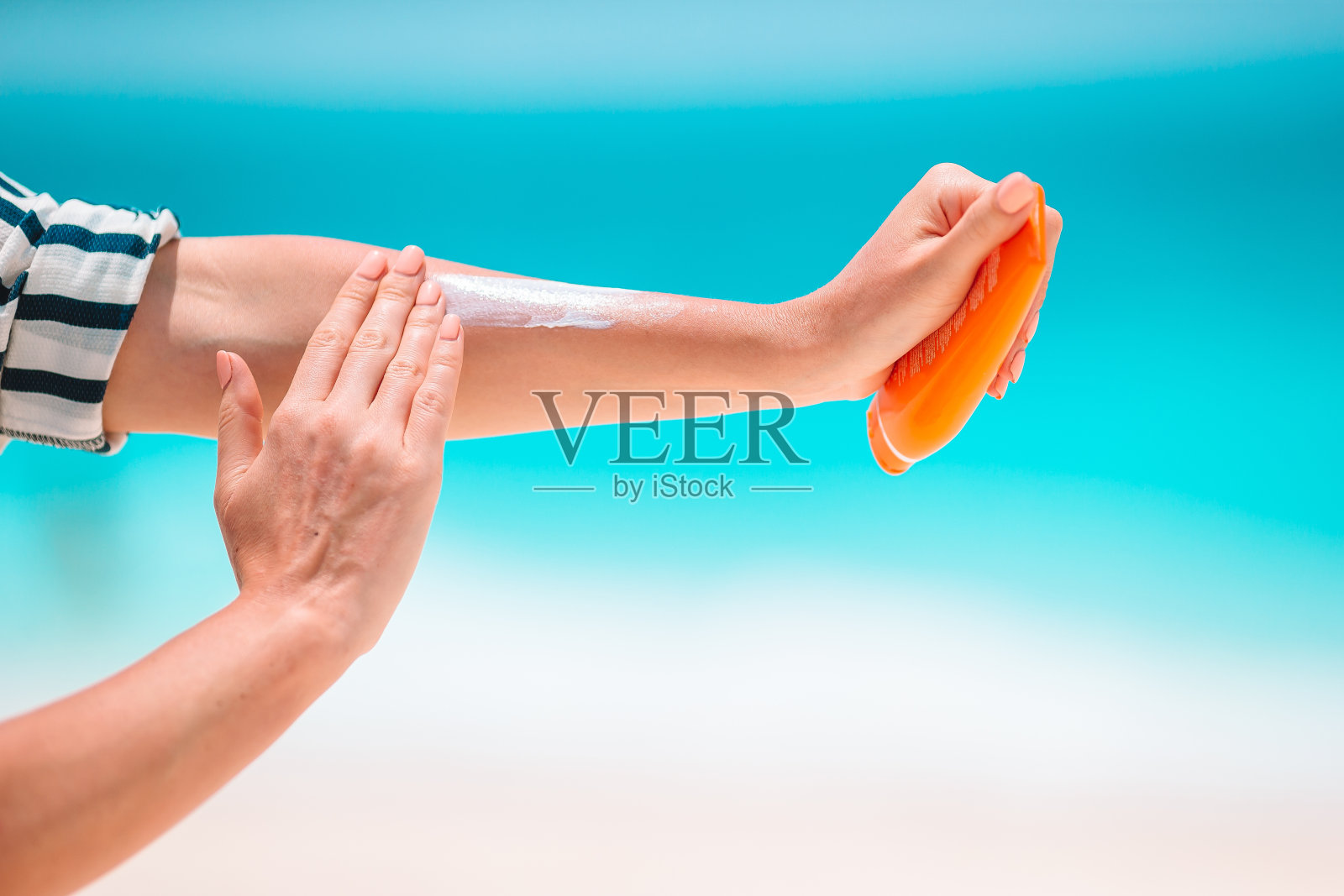 女性手持防晒霜瓶子,背景为蓝绿色海水照片摄影图片