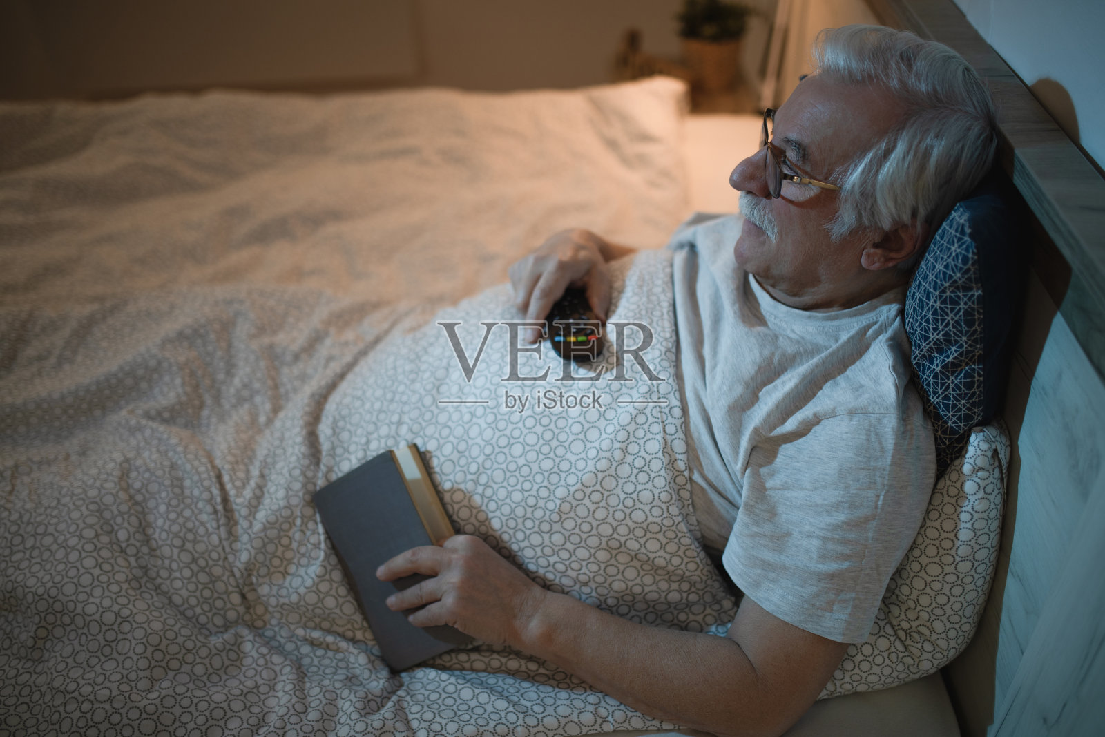 微笑的老人看电视,而休息在床上晚上。照片摄影图片