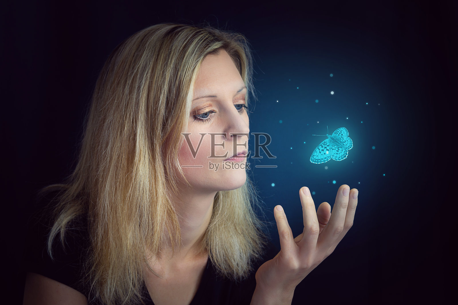 手捧蓝色蝴蝶的年轻金发女子。黑色背景上的蝴蝶摄影作品照片摄影图片
