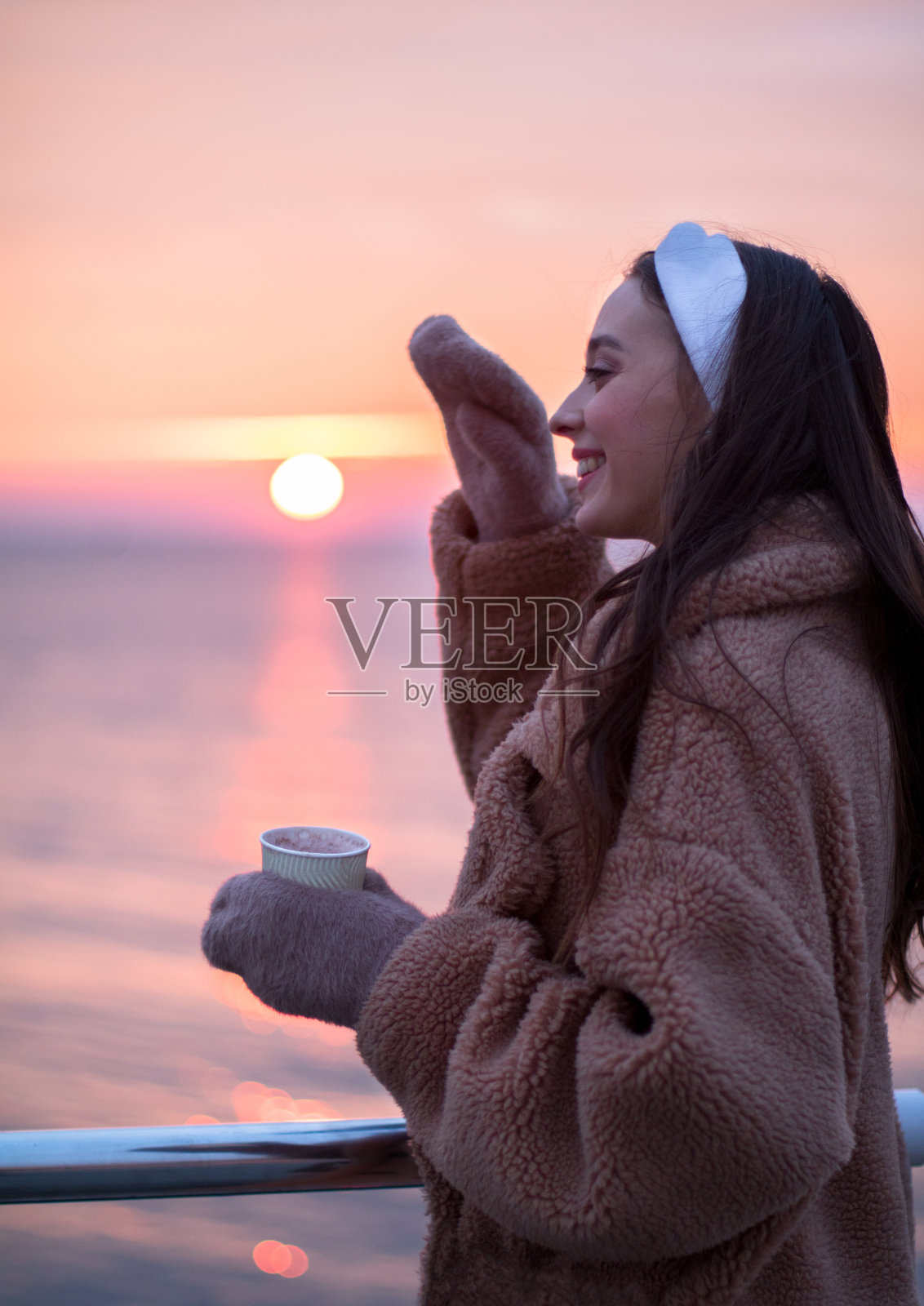 年轻的女孩在裘皮大衣与一杯热饮钦佩的风景红色日出在海上散步照片摄影图片