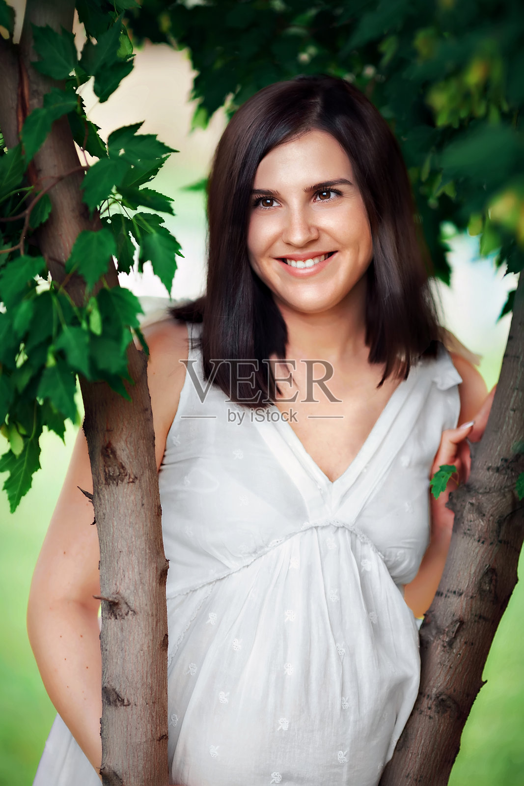 孕妇身穿白裙站在树旁,幸福地等待宝宝的降生照片摄影图片