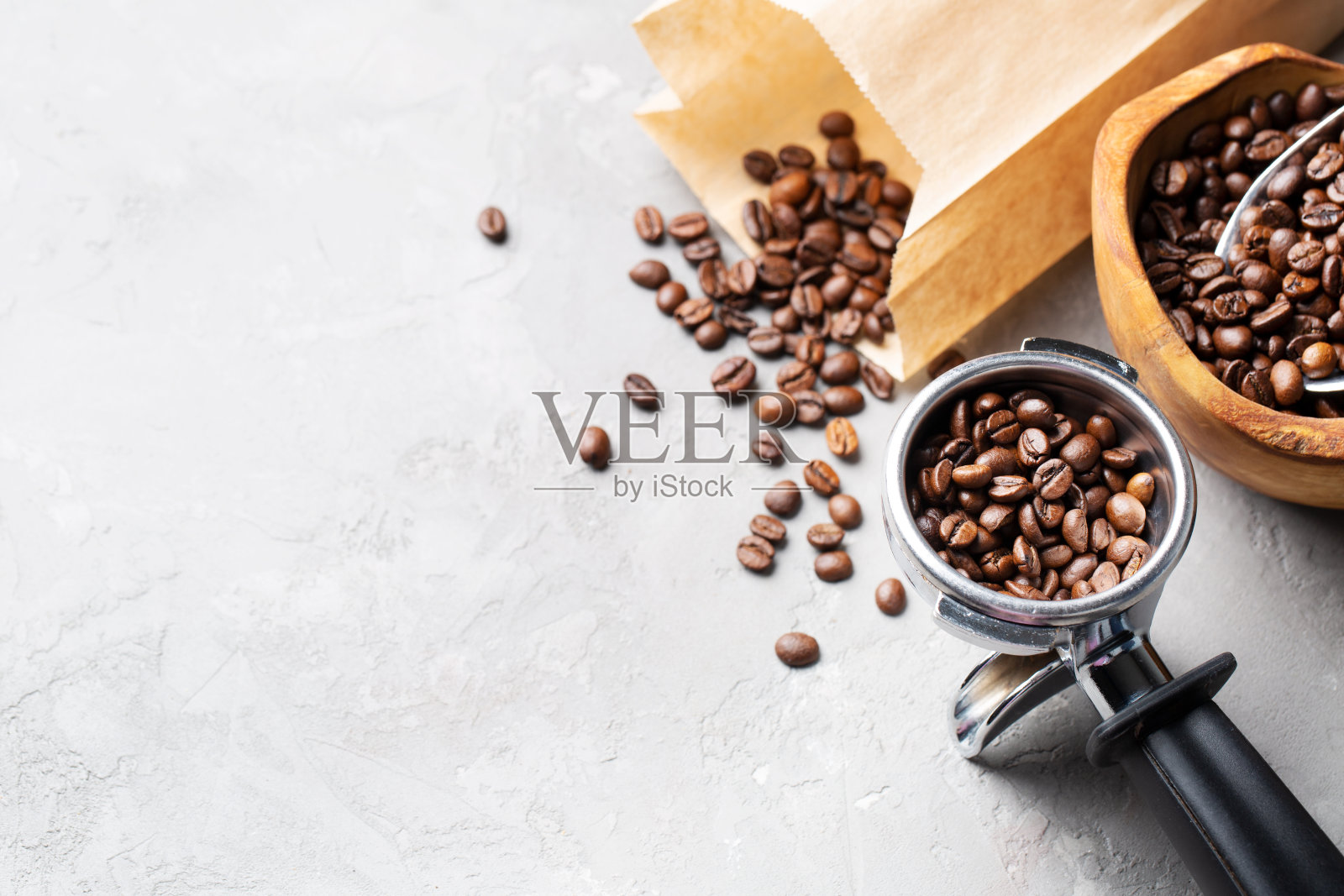 咖啡豆装在一个橄榄木做的木碗里,装在一个纸袋里,还有一个浅灰色背景的金属过滤器。空间的文本。照片摄影图片