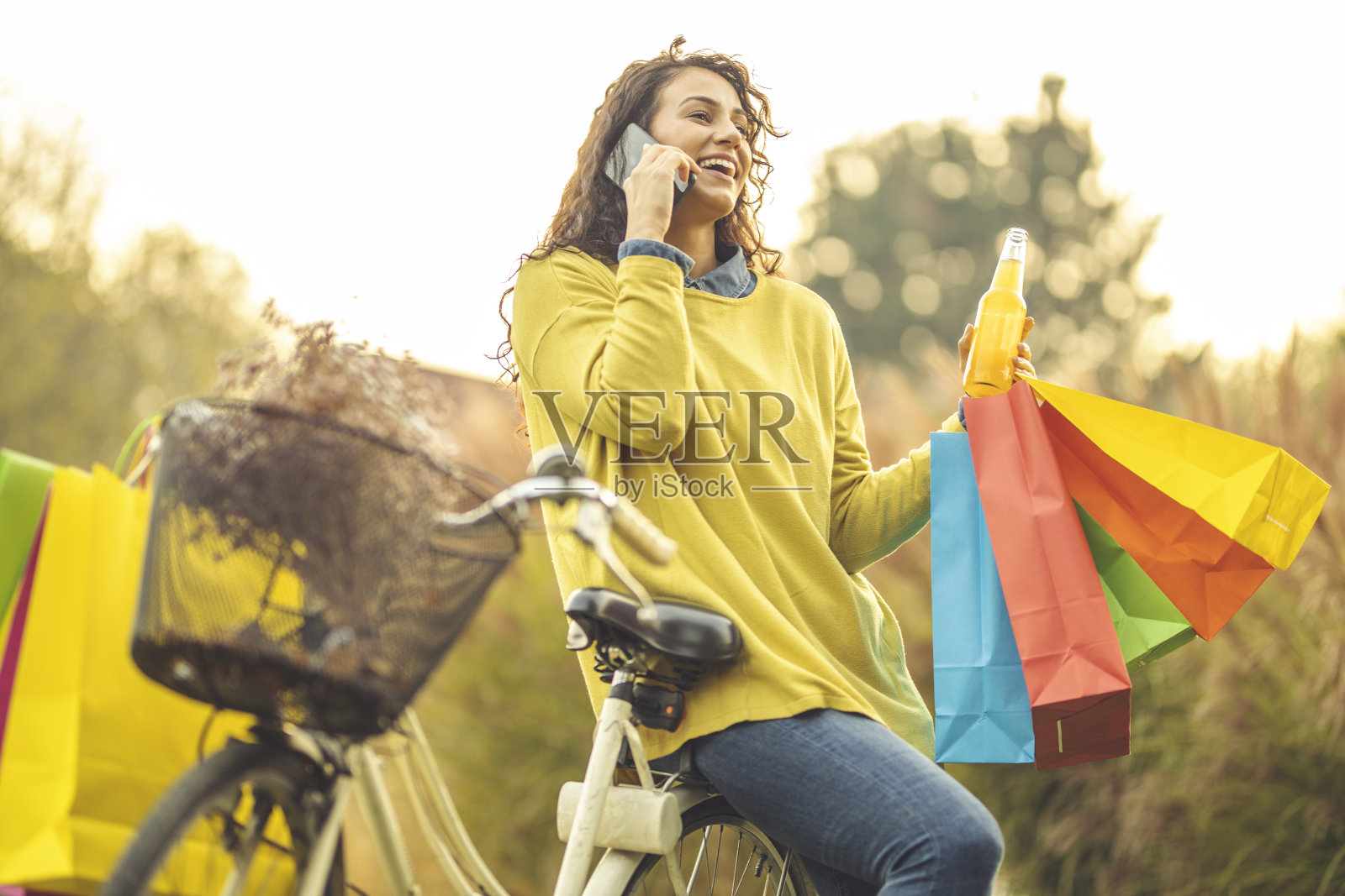 女人喝果汁,拿购物袋和使用手机照片摄影图片