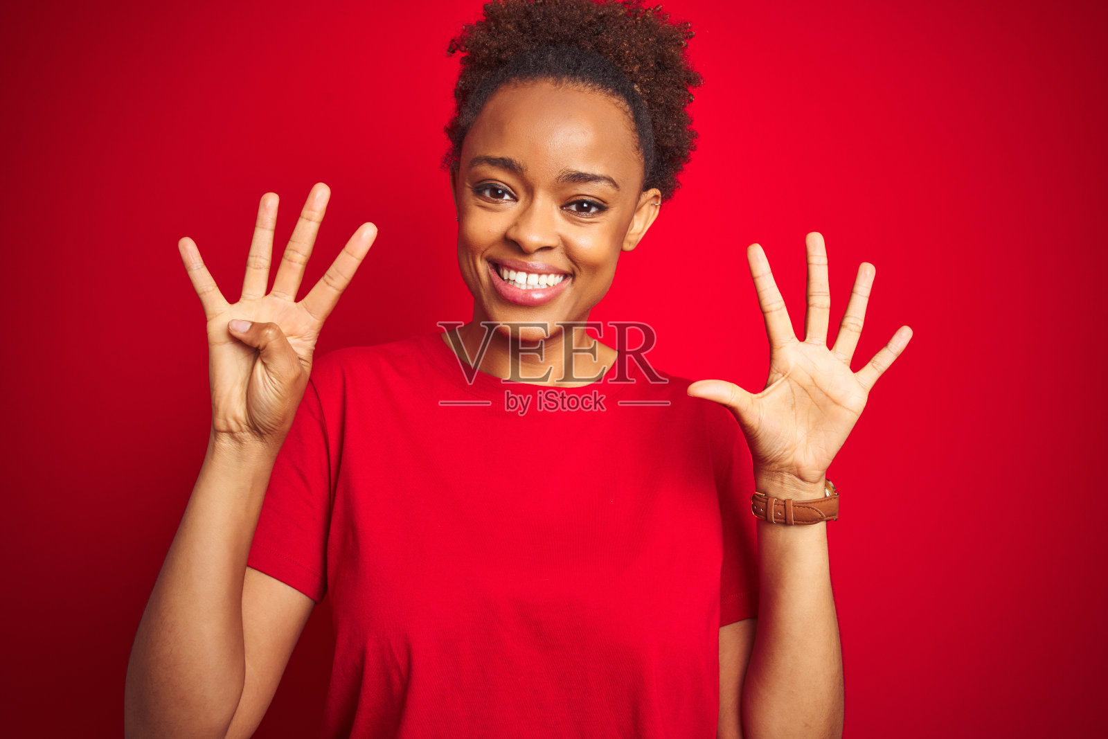 年轻漂亮的非裔美国妇女在孤立的红色背景下,自信而快乐地笑着,用手指指着上方,比出数字“九”。照片摄影图片