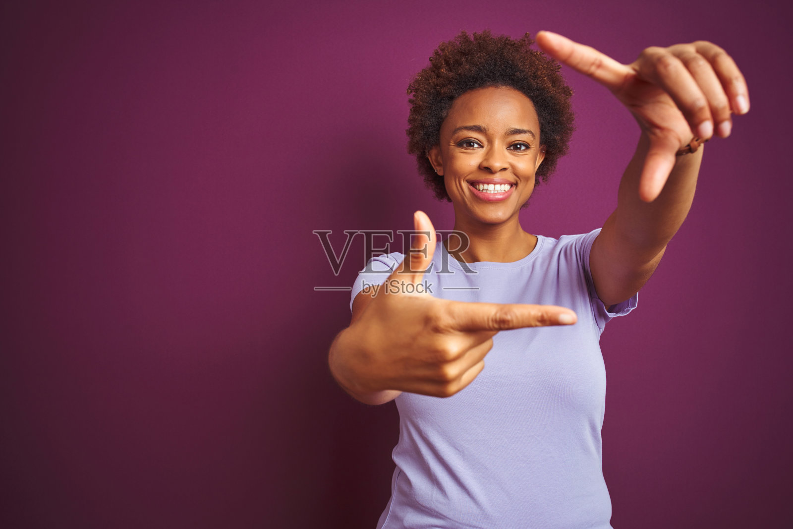 年轻漂亮的非裔美国妇女,蓬松发型,在孤立的紫色背景下微笑,用手和手指做出框架,面带幸福的表情。创意和摄影概念。照片摄影图片