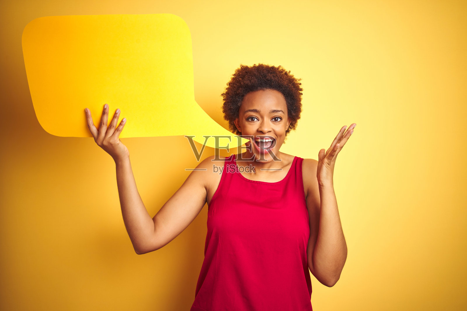 年轻的非裔美国女人在黄色背景下手持对话气泡,非常高兴和兴奋,面带微笑,举起双手,庆祝胜利照片摄影图片