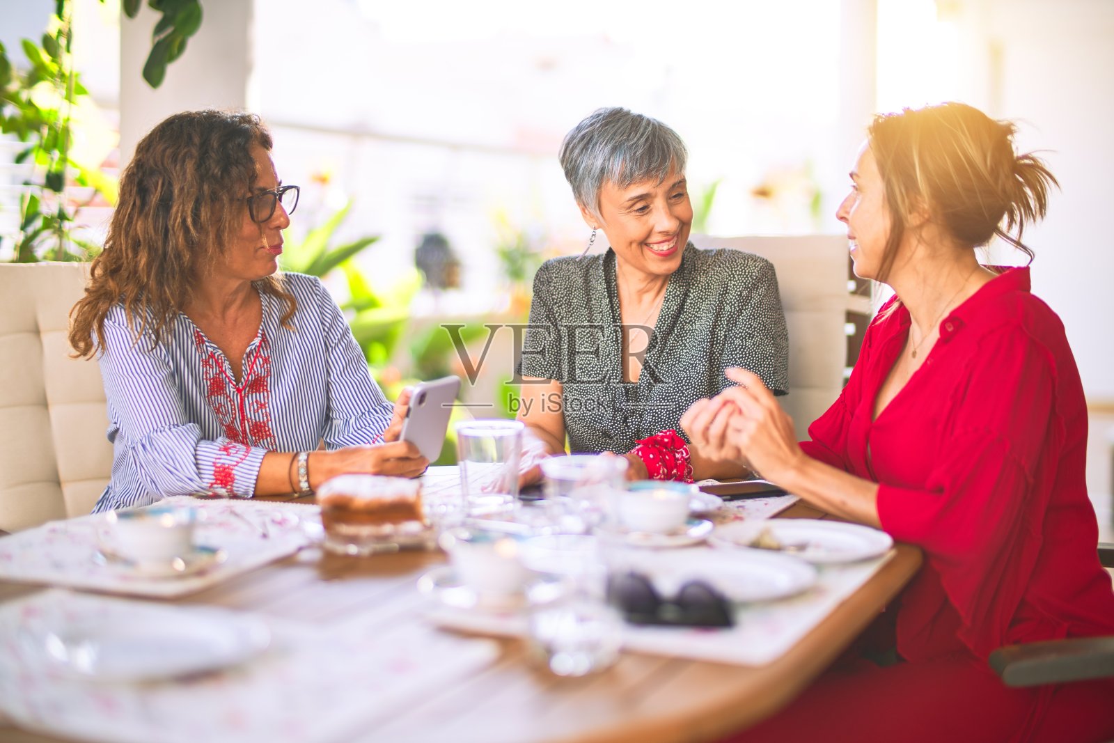 遇见中年妇女吃午饭喝咖啡。阳光明媚的日子里,成熟的朋友在家里用智能手机微笑照片摄影图片