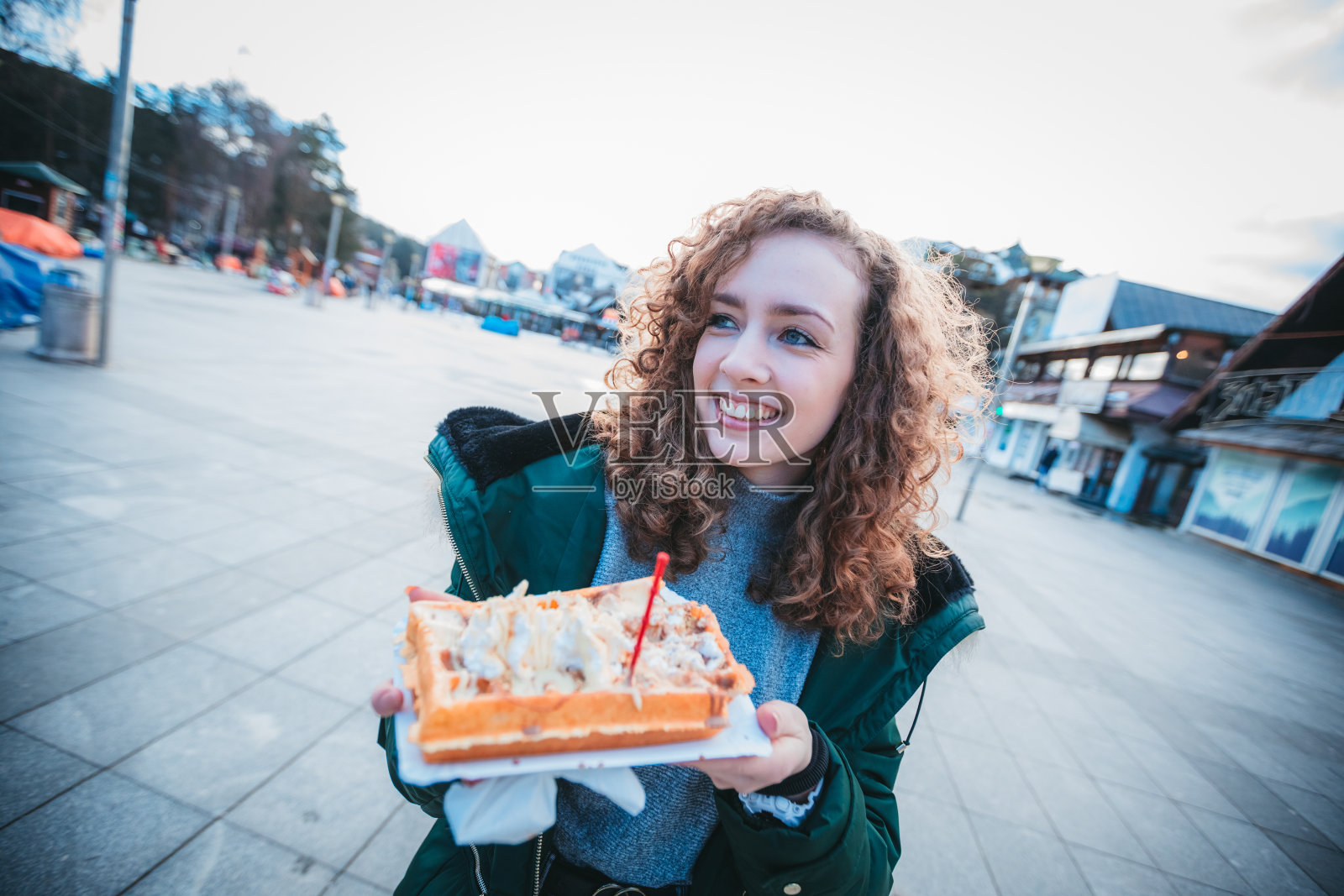 在城市广场吃华夫饼的美丽卷发女孩照片摄影图片