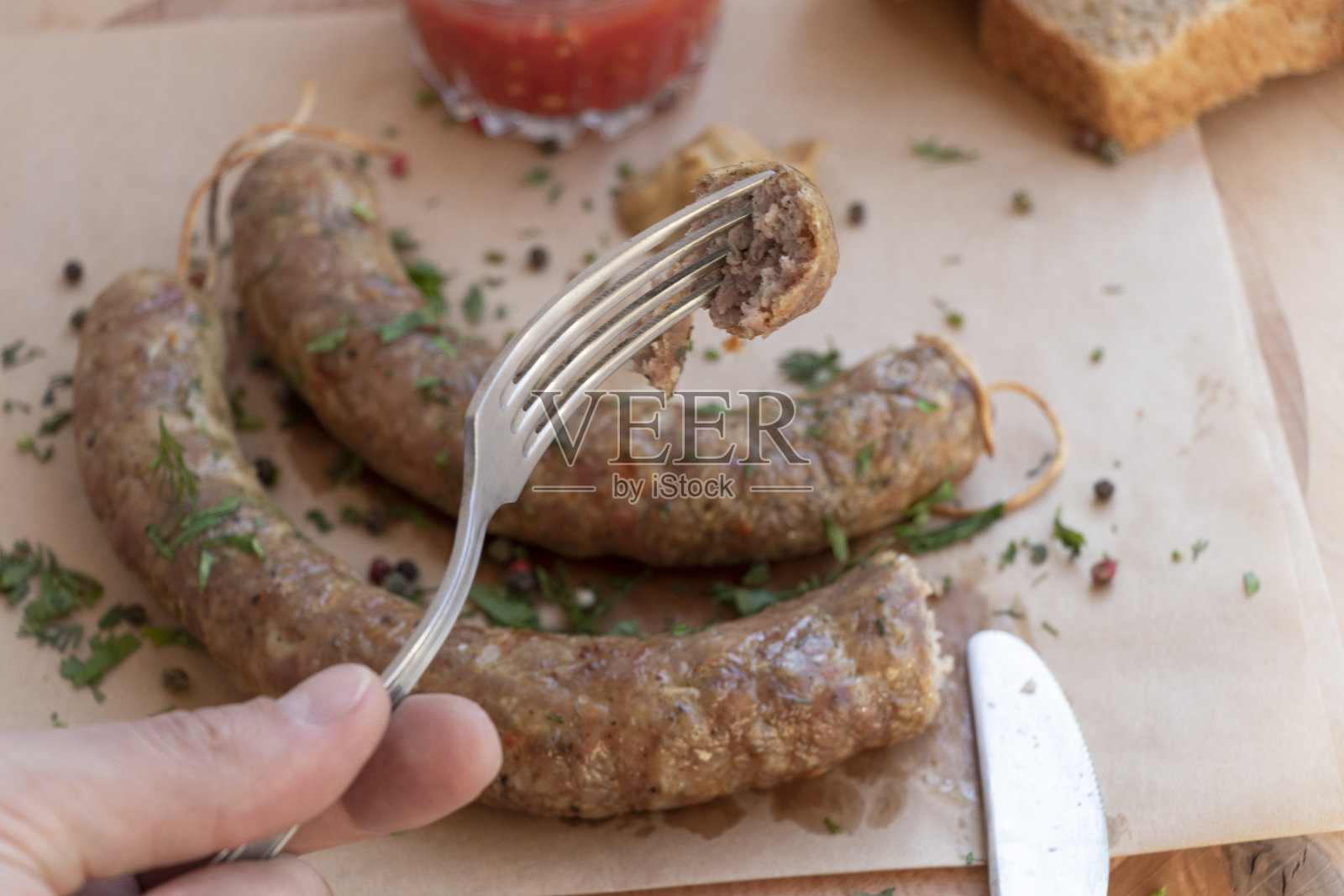 自制的纸香肠配上芥末和番茄酱。餐具和面包。俯视图上的一个木制背景。手拿着照片摄影图片