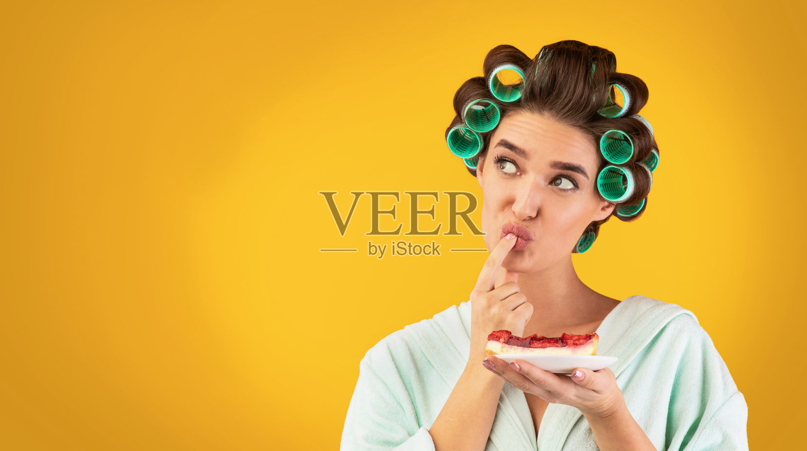 饥饿的家庭主妇品尝蛋糕站在黄色的工作室背景,全景照片摄影图片