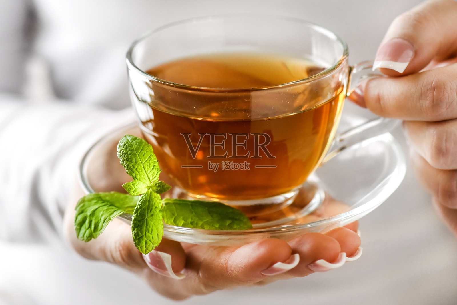 女人手里拿着一杯热茶。茶在清澈的玻璃杯在美丽的手照片摄影图片