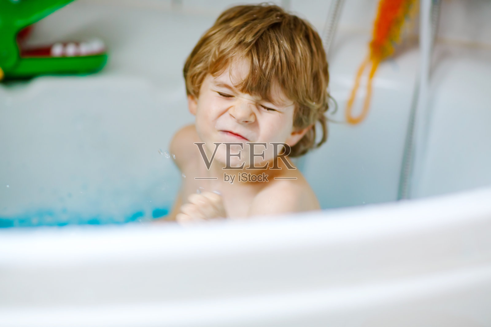 可爱的小孩在家里的浴缸里玩水。可爱的快乐健康的学前班小男孩玩得很开心,洗头发和头,用肥皂泼水照片摄影图片