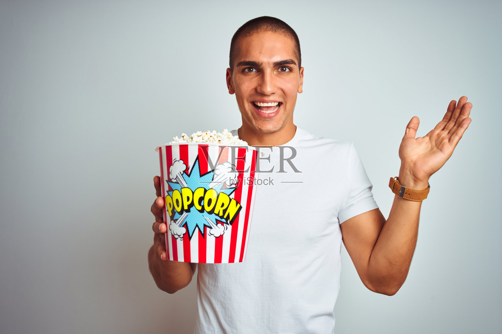 年轻英俊的男子吃着爆米花在白色孤立的背景非常高兴和兴奋,胜利者的表情庆祝胜利尖叫着大大的微笑和举起手照片摄影图片