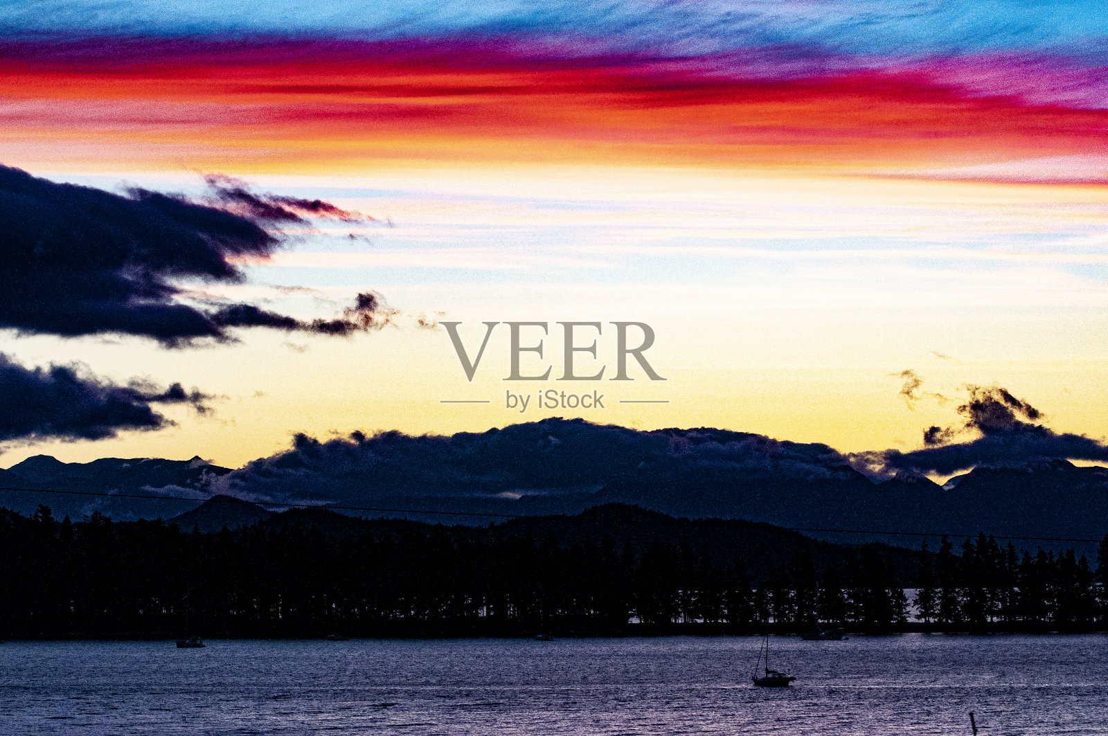 戏剧性的日落与红色,黄色和蓝色的云在山,水和树的剪影照片摄影图片