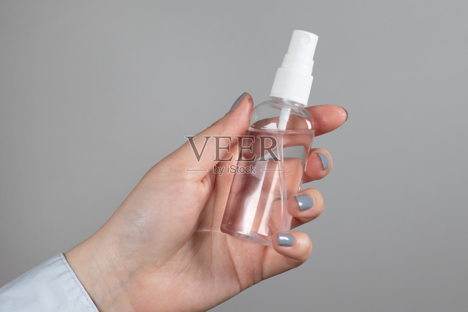 女士的手拿着一个塑料瓶,上面有消毒液喷雾,灰色背景去掉。一种预防冠状病毒、大流行的工具照片摄影图片
