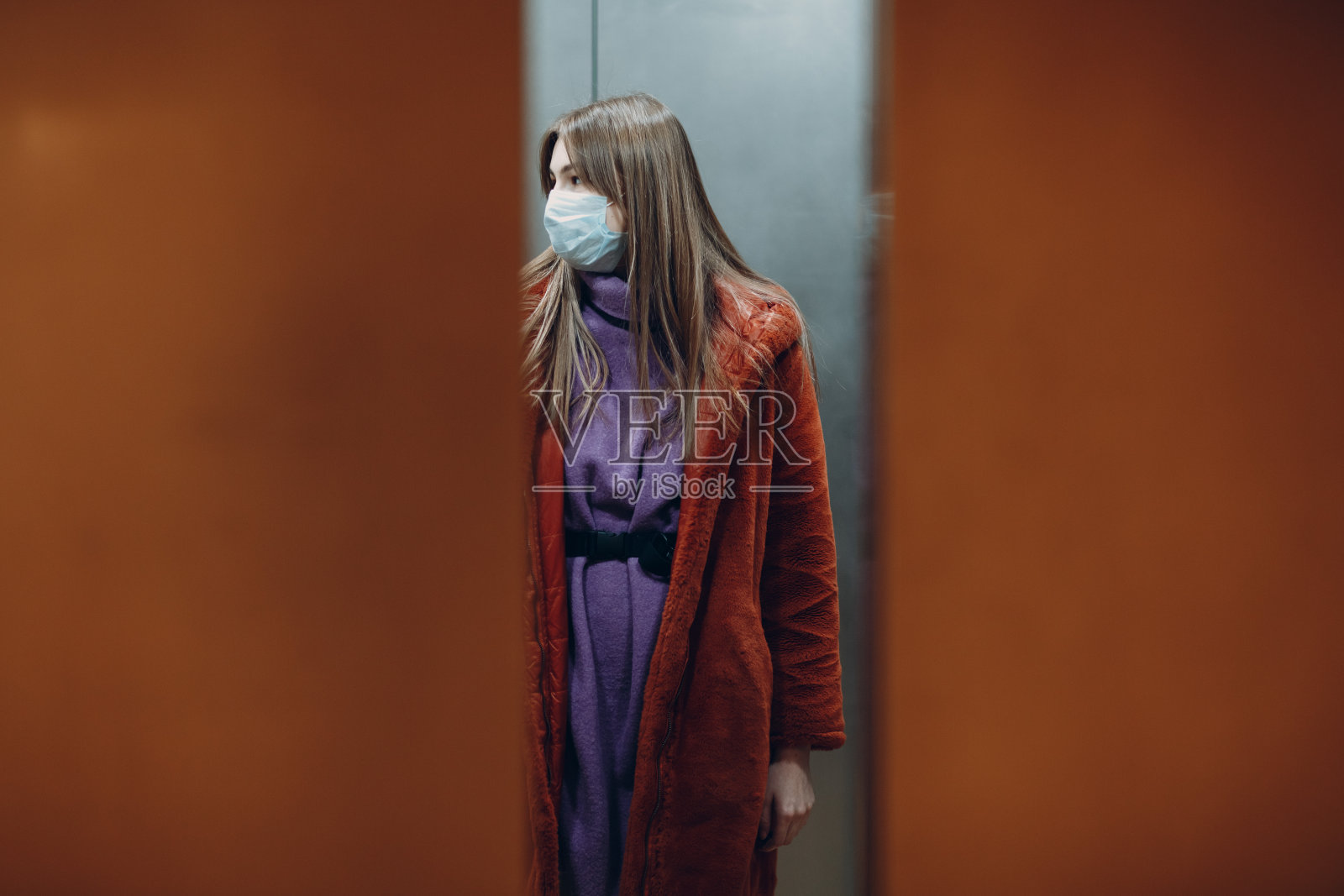 年轻女子戴着医用口罩站在电梯里。门正在关闭。冠状病毒- COVID-19大流行概念。照片摄影图片