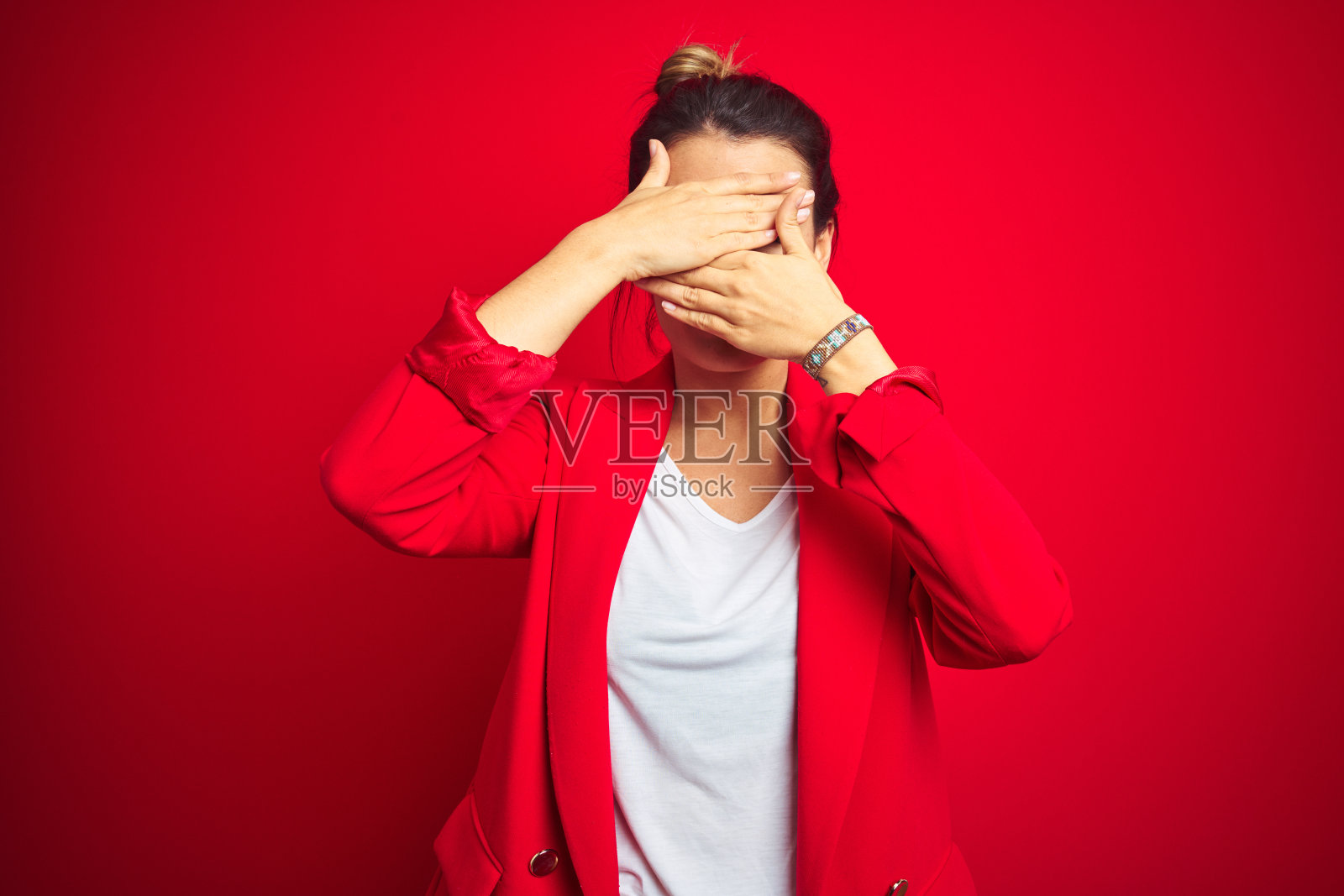 在红色背景下用手捂住眼睛和嘴巴,感到惊讶和震惊的年轻漂亮女商人照片摄影图片
