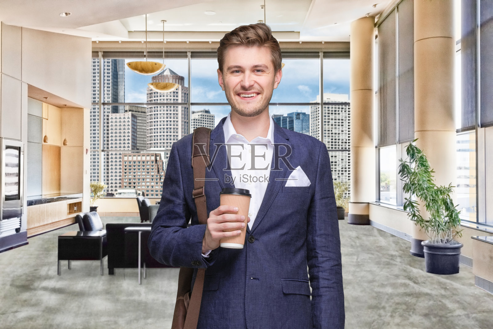 男商人站在办公室里,穿着邮差包,拿着咖啡杯照片摄影图片