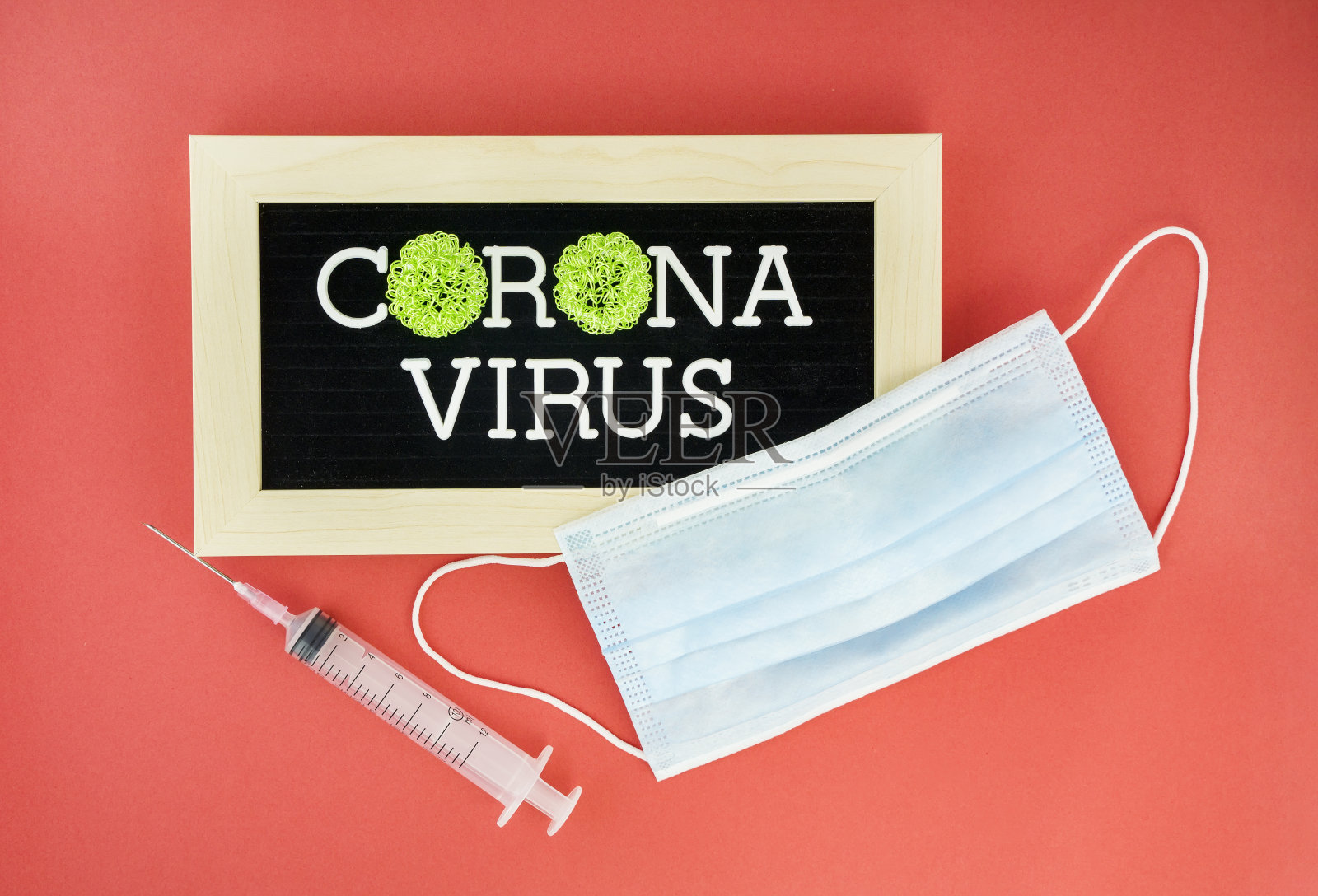 红色背景上冠状病毒字字母,呼吸保护口罩旁边的注射器,医疗保健和医疗概念。照片摄影图片