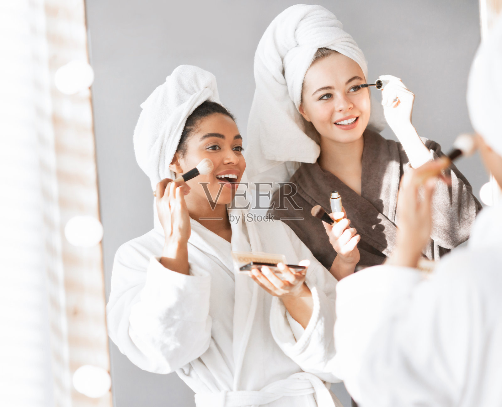 迷人的年轻女子站在镜子前,涂抹粉底照片摄影图片