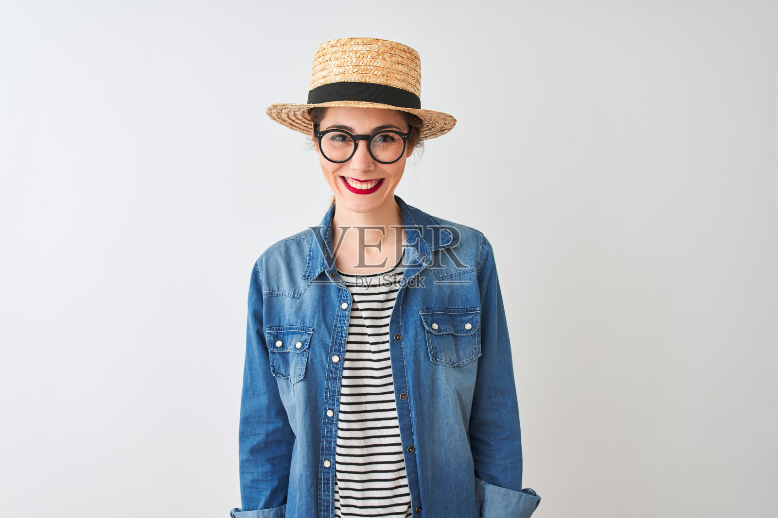 红发女人戴着牛仔衬衫、眼镜和帽子,在白色背景前露出快乐而酷酷的微笑,幸运的人照片摄影图片