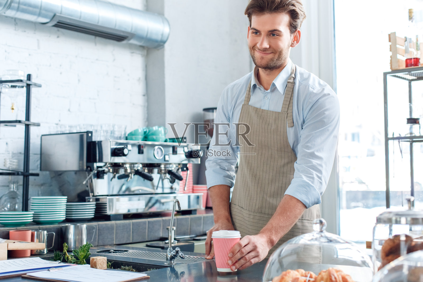 咖啡的激情。年轻的咖啡师微笑着给顾客一杯热咖啡照片摄影图片
