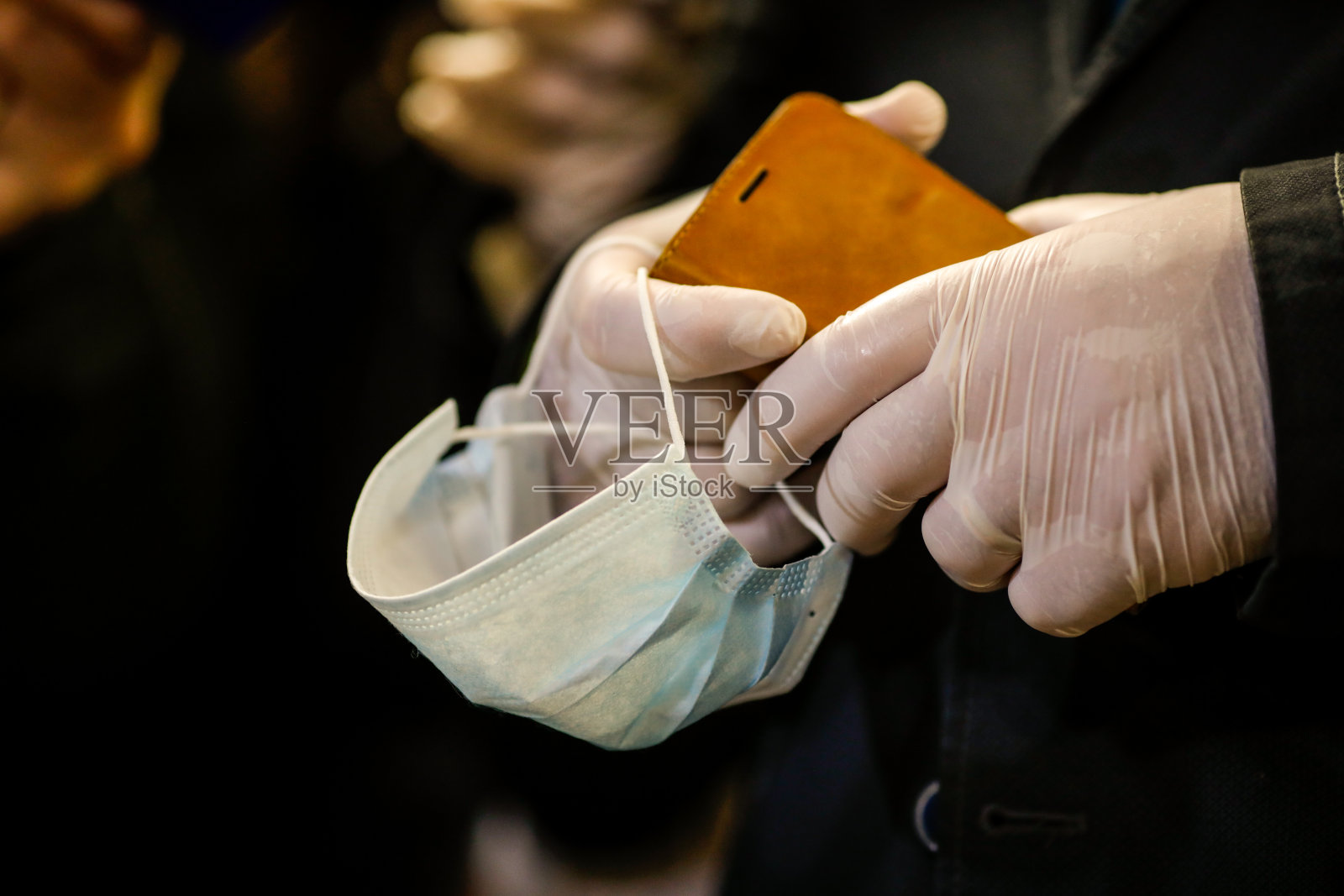 一名男子戴着外科手套,手持手机和口罩,以防止COVID-19传播。照片摄影图片