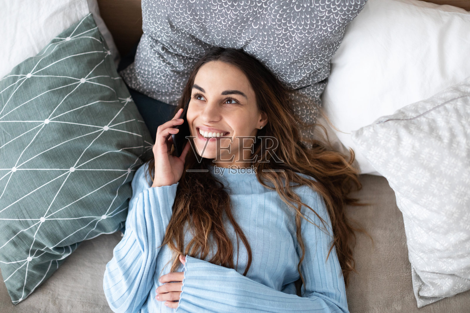 年轻漂亮的女人躺在沙发上打电话。照片摄影图片