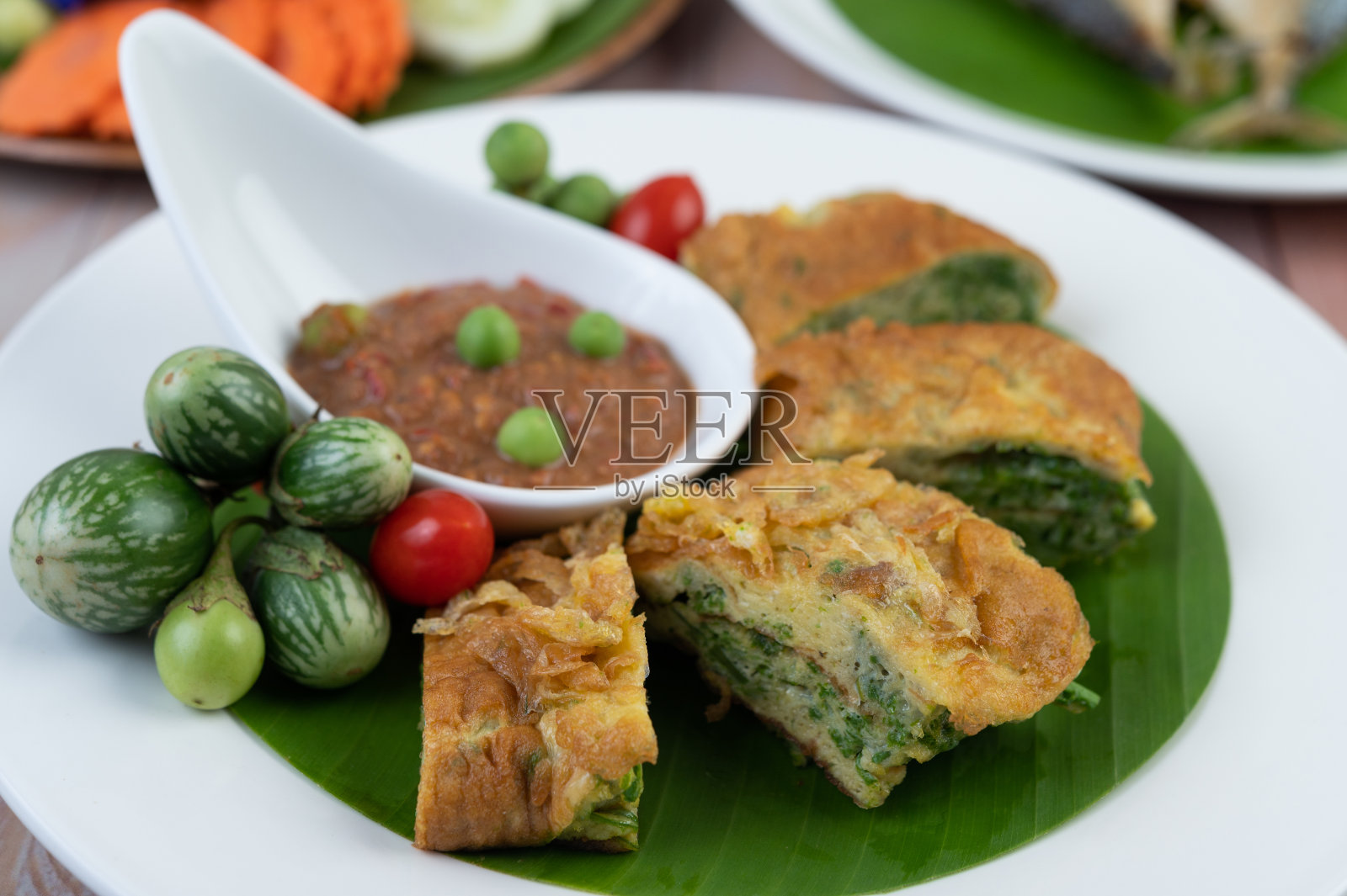 虾酱、煎蛋卷、茶碗和茄子一起放在一个白色的盘子里,放在木地板上。照片摄影图片