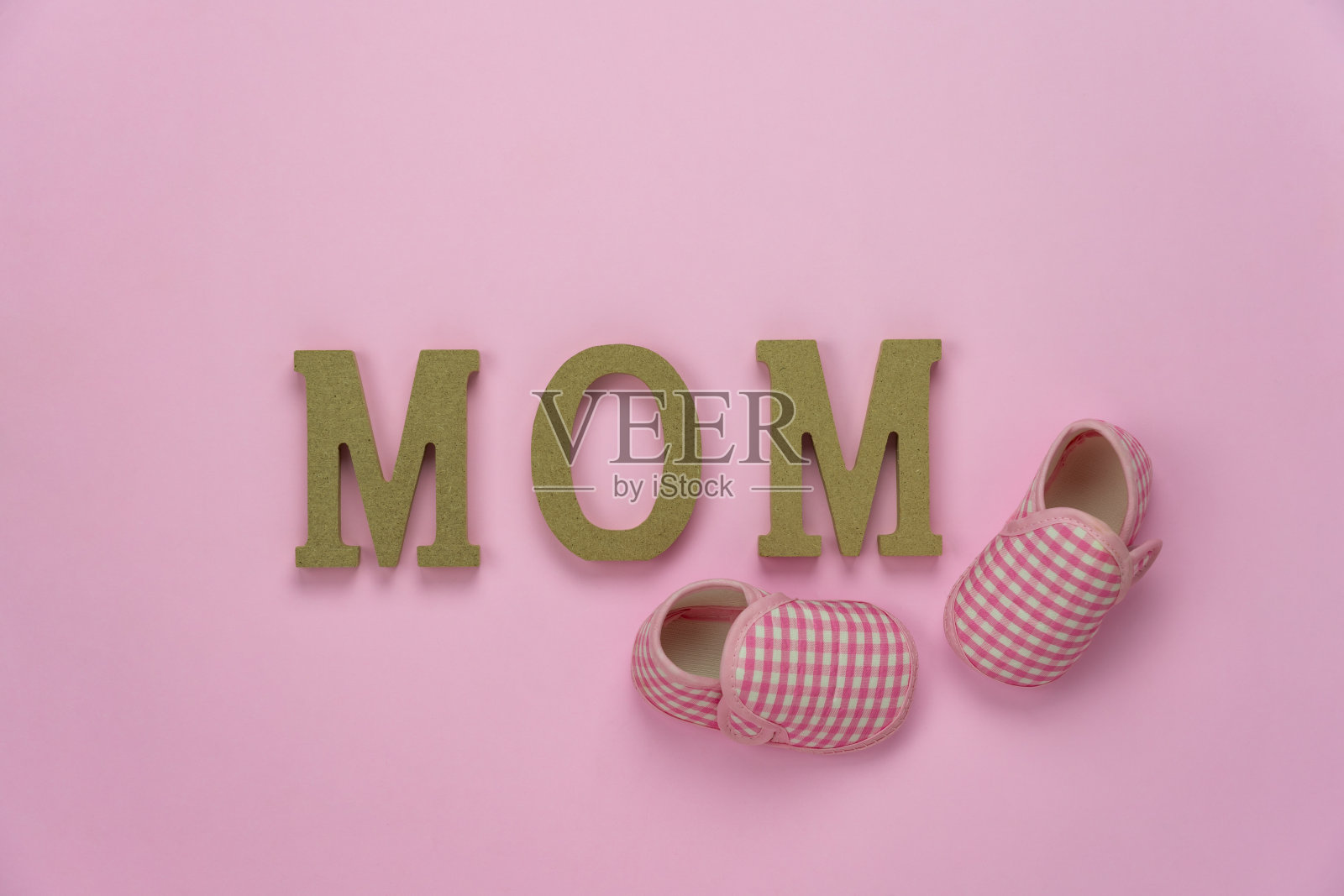 俯视图航拍装饰母亲节节日背景概念。平躺婴儿鞋和妈妈文本在现代美丽的粉红色纸在家庭办公办公桌。粉彩色调创意设计。照片摄影图片