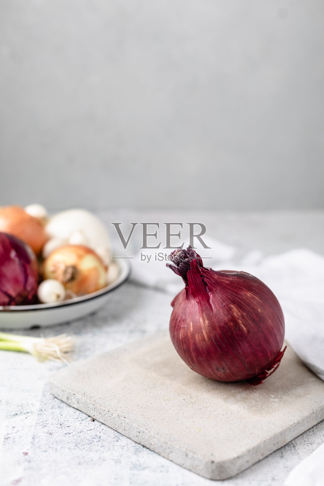 整颗红洋葱在水泥切菜板上,背景中有几种洋葱失焦照片摄影图片