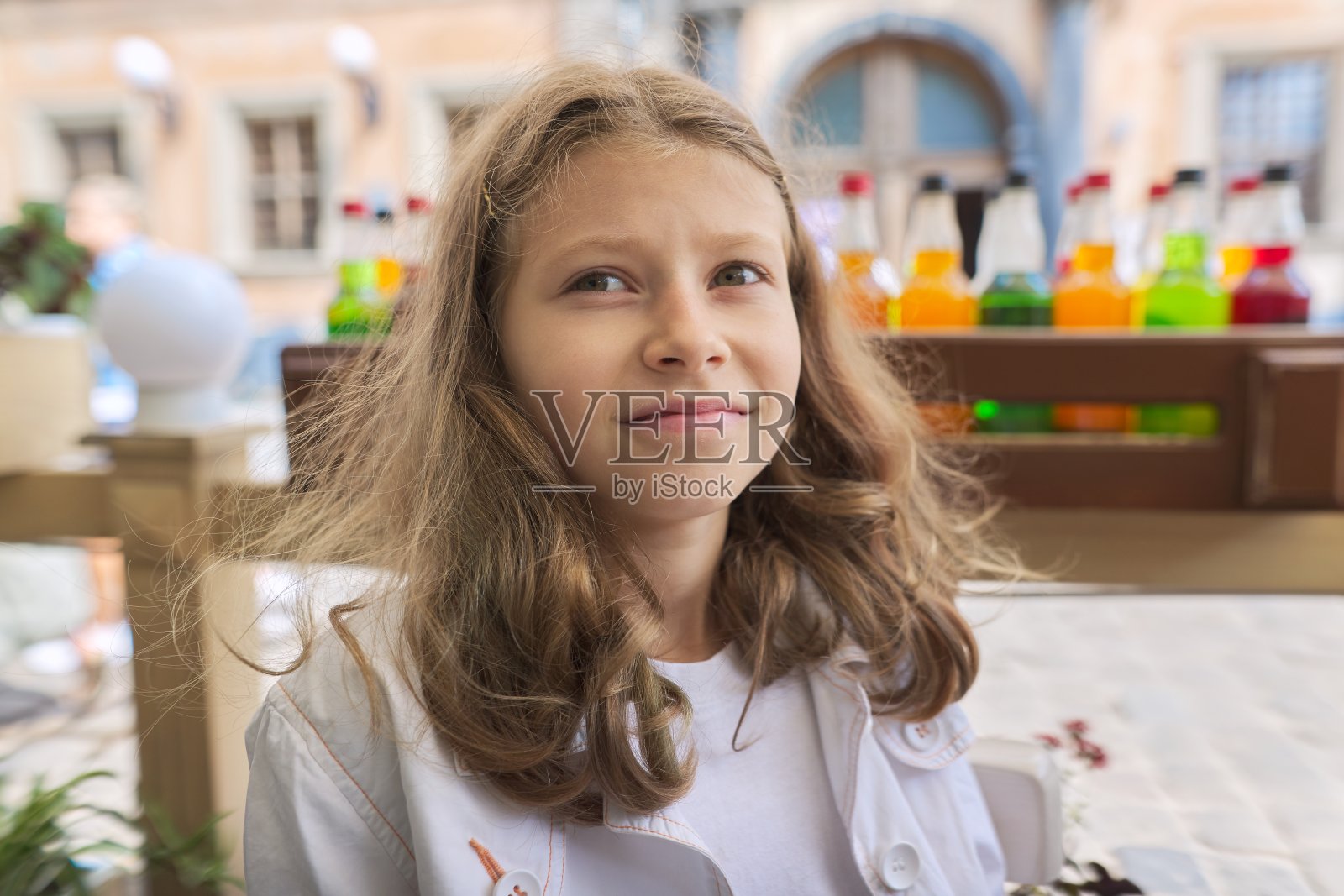 9-10岁女孩肖像:坐在城市户外咖啡馆里微笑的金发女孩照片摄影图片