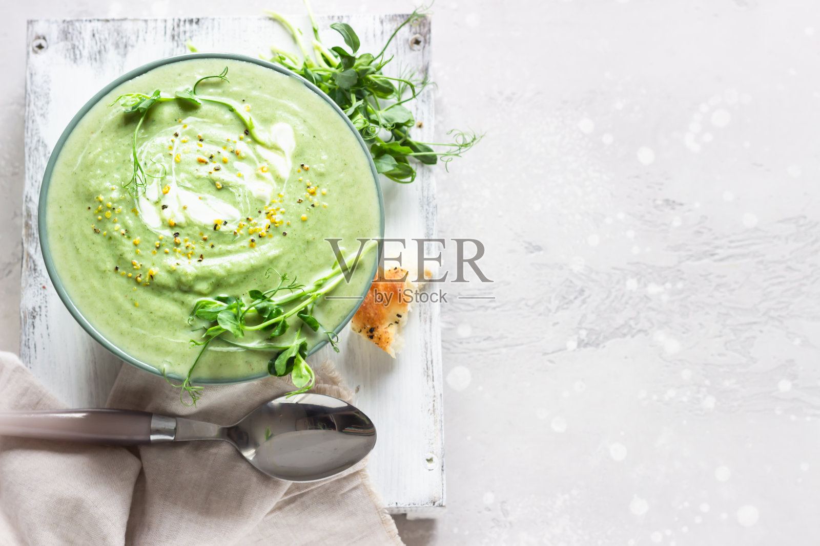 春季蔬菜奶油汤在一个碗与微型绿色蔬菜,奶油和新鲜佛卡夏在一个明亮的背景。健康素食理念。照片摄影图片