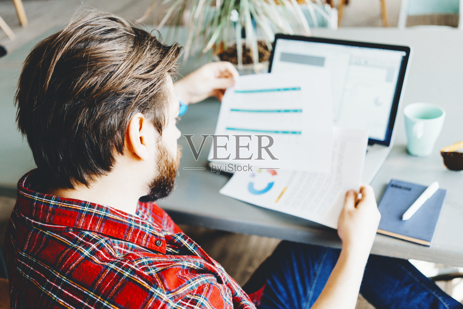 年轻的胡茬男人在明亮的大办公室里用笔记本电脑工作,比较月度统计数据照片摄影图片