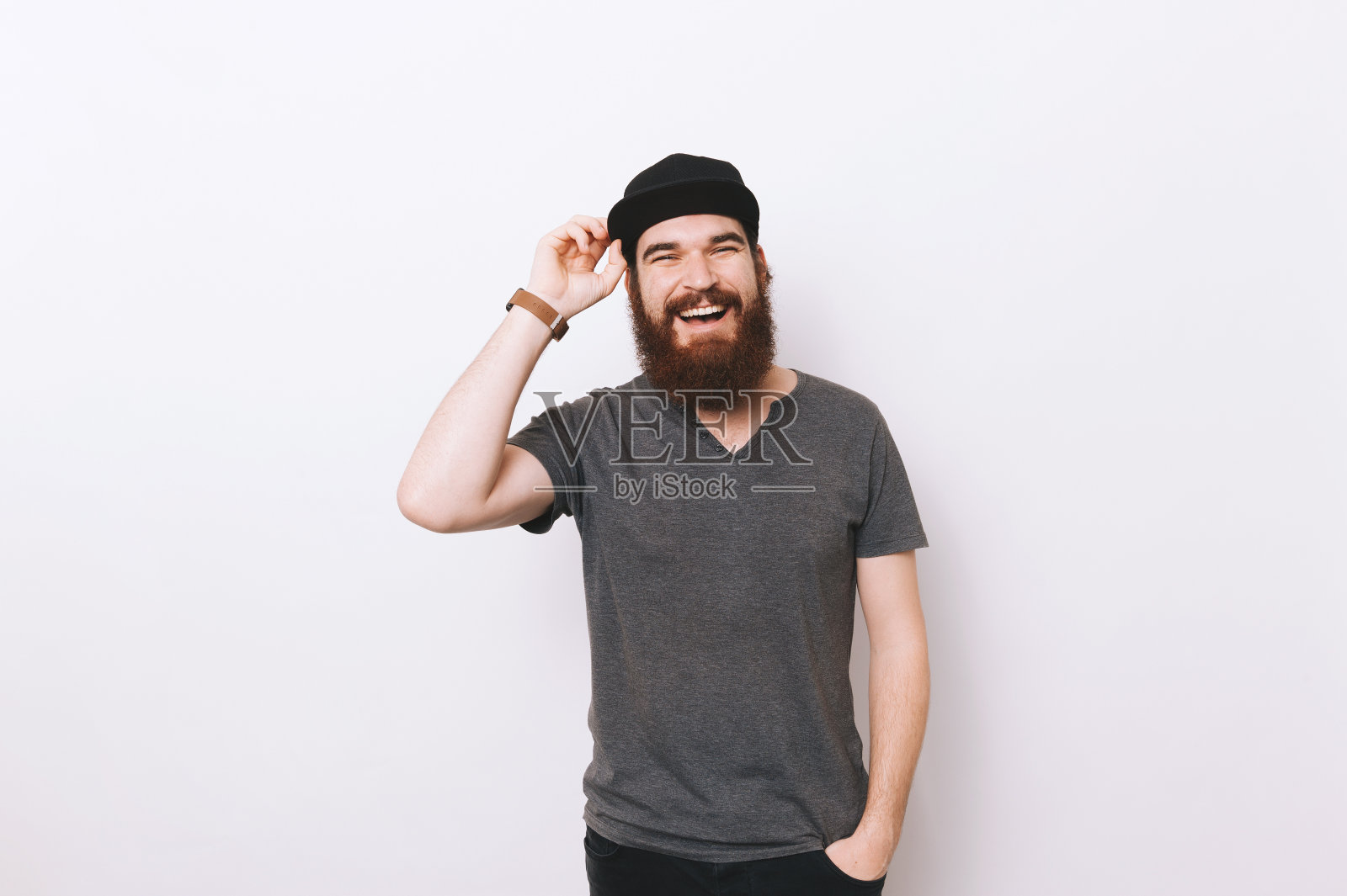 肖像快乐的大胡子男人的手在口袋里,拿着他的帽子照片摄影图片