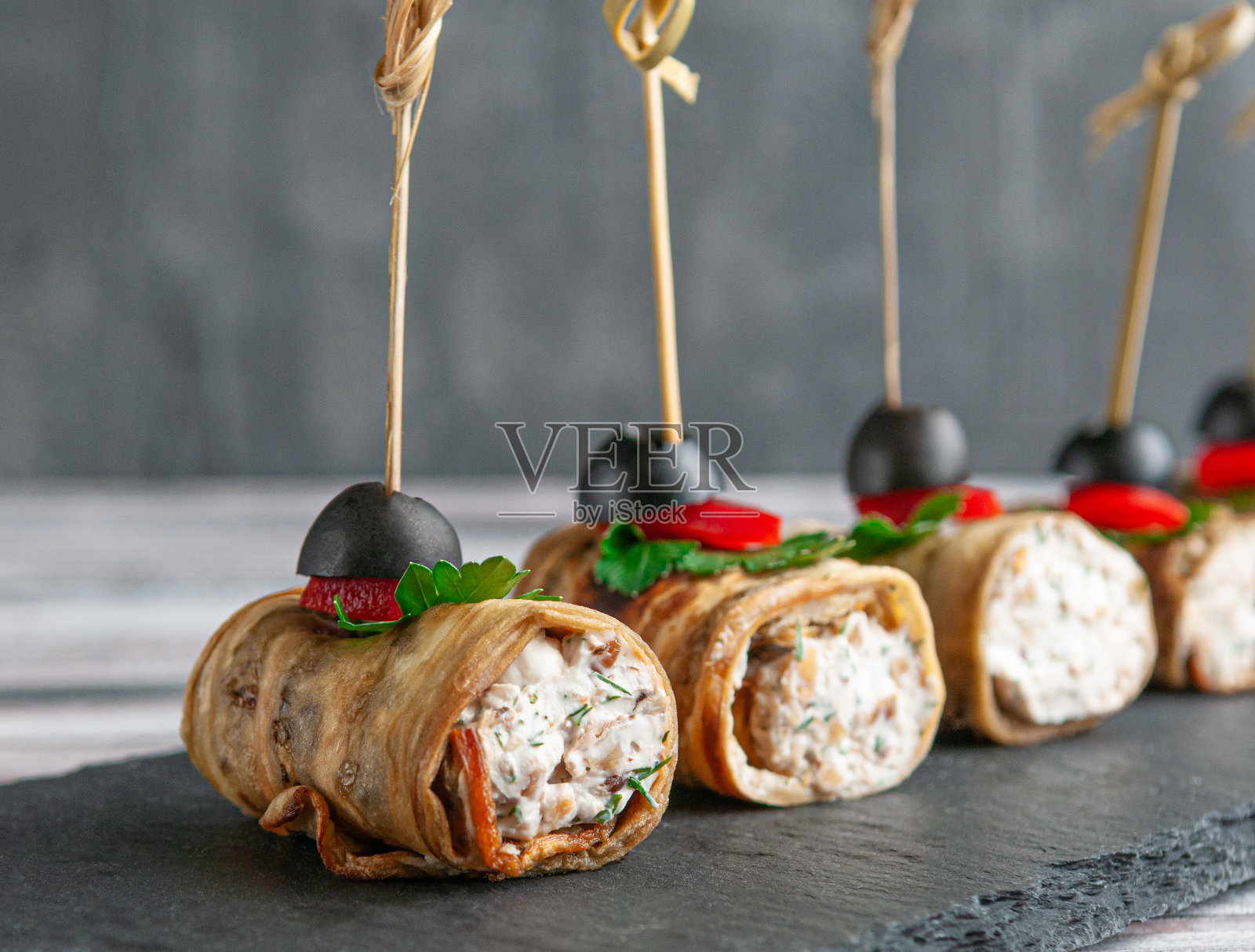 塞满奶酪和香草的油炸茄子。配以甜椒、欧芹和橄榄。在一块黑色的石板上。灰色的背景。特写镜头。照片摄影图片