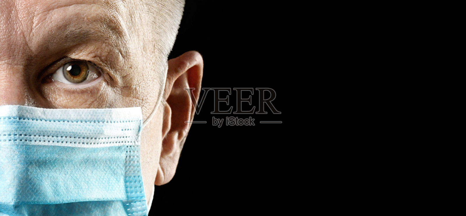 黑色背景下,戴着医用口罩的男人看着镜头特写,留白照片摄影图片