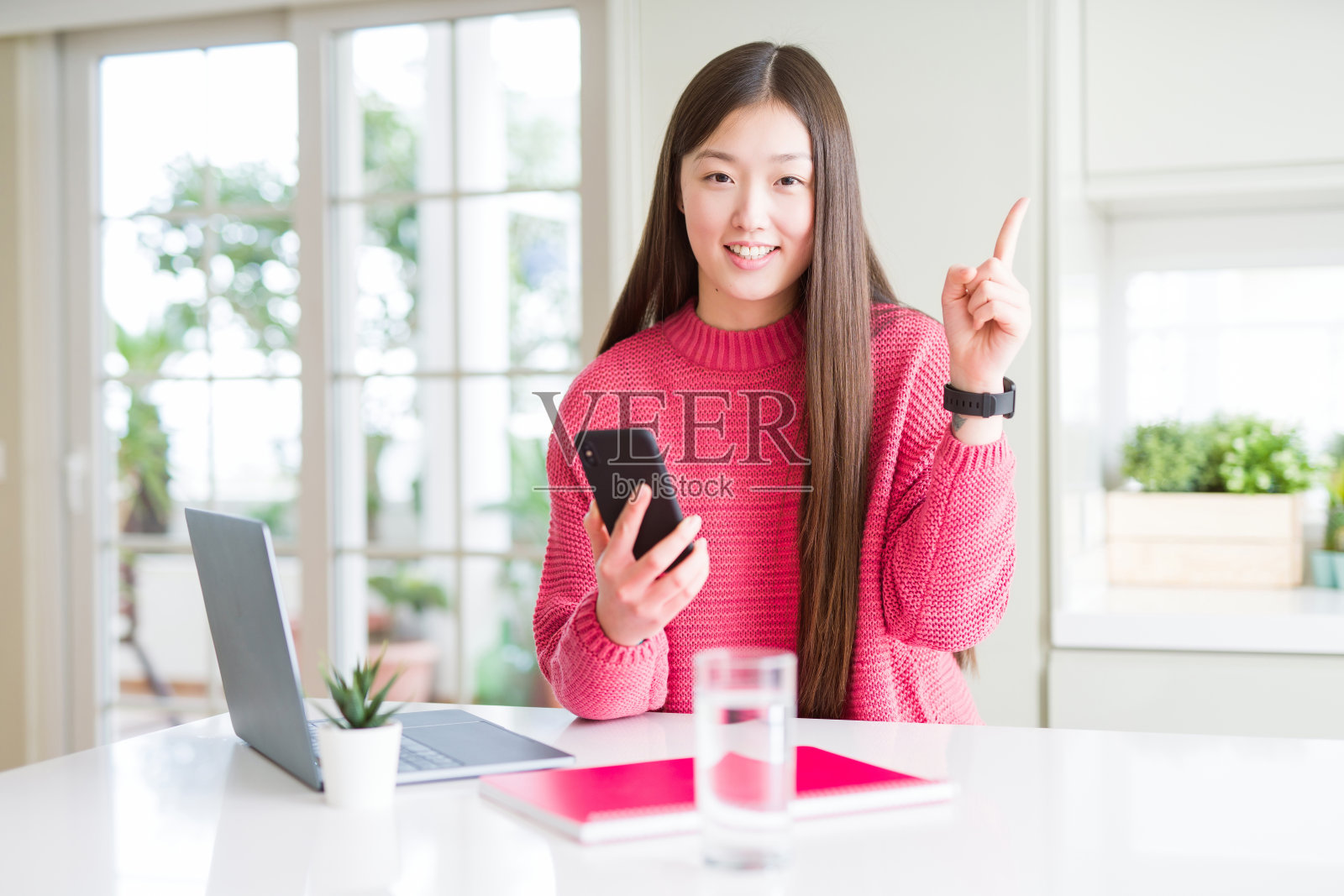 美丽的亚洲女学生使用笔记本电脑和智能手机非常高兴的指向与手和手指的一边照片摄影图片