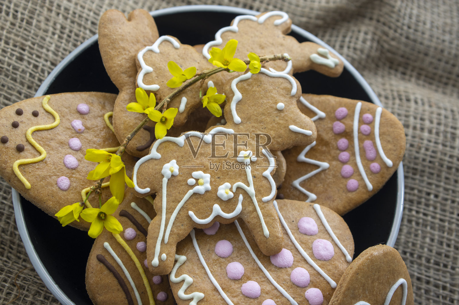 复活节的小甜饼盛在盘子里,桌上铺着黄麻桌布,春季的一组彩色姜饼上涂着糖果照片摄影图片