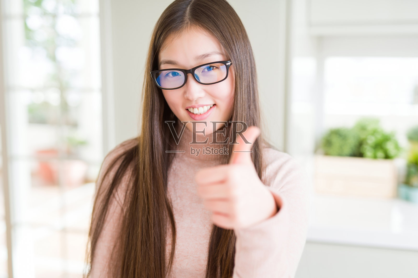 美丽的亚洲女人戴着眼镜做快乐的拇指手势与手。赞许的表情看着镜头,表示成功。照片摄影图片
