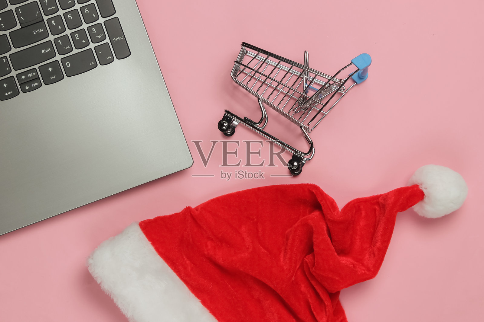 带圣诞帽的笔记本电脑,粉色背景的购物车。圣诞购物。俯视图照片摄影图片