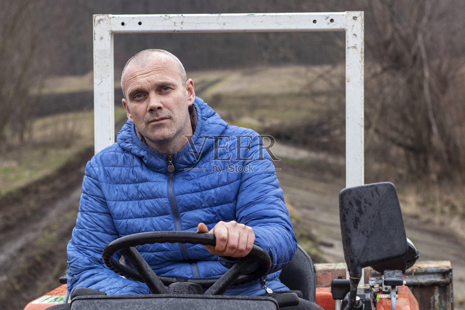 雨中驾驶无 cab 的拖拉机的疲惫男子肖像照片摄影图片