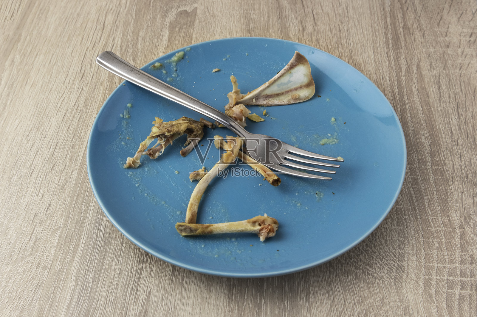 木桌上放着一个脏兮兮的盘子,上面放着叉子和兔子骨头。照片摄影图片