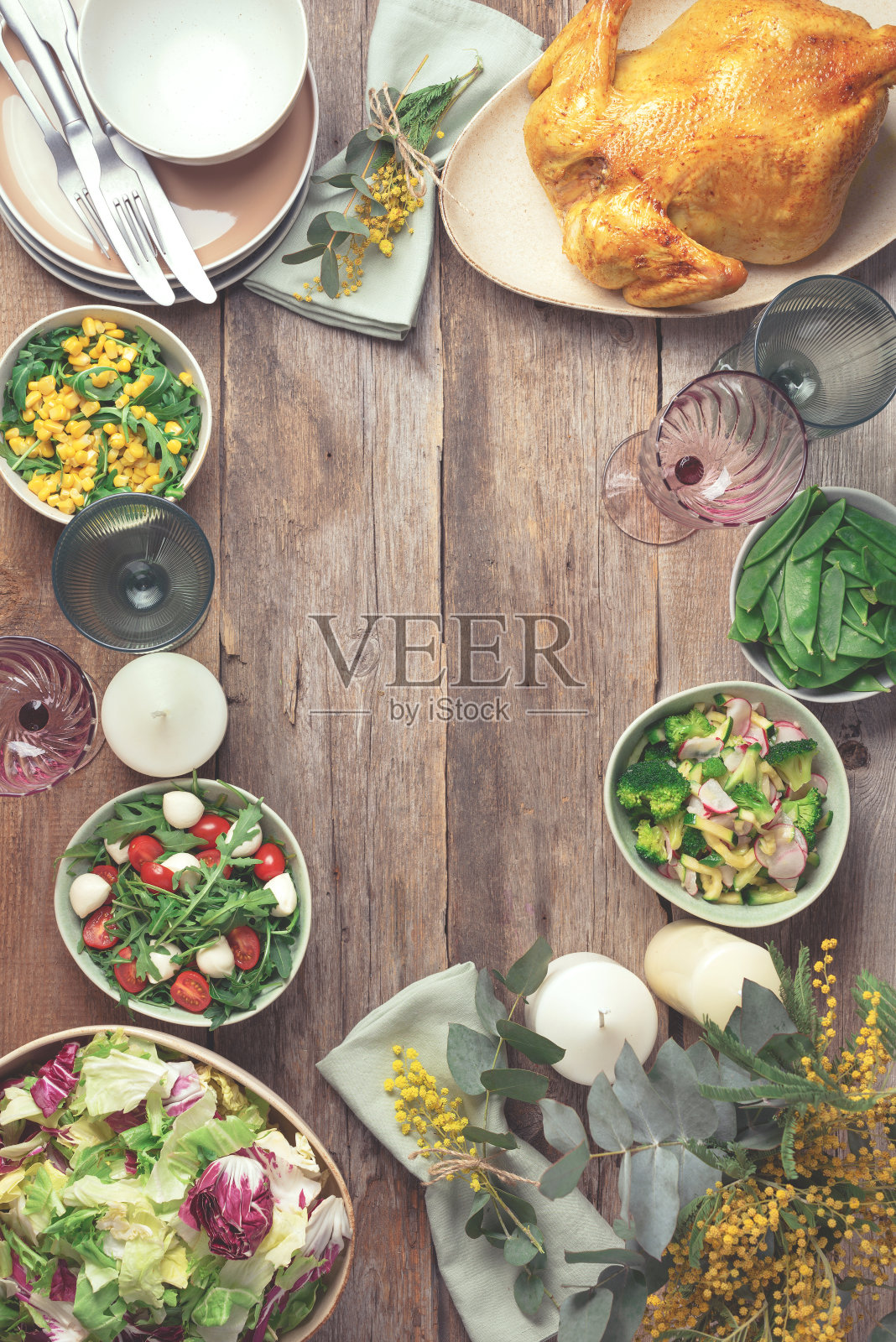 节日家庭餐桌。提供盘子,碗与沙拉和蔬菜菜肴,零食,整个烤鸡,桉树,含苞欲放的花木制背景。情人节,妇女节,母亲节照片摄影图片